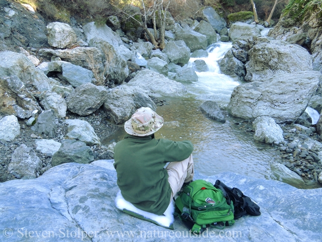 hiker sitting on rocks in front of waterfall