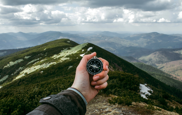 hand holding compass in mountains Photo by Anastasia Petrova, Unsplash